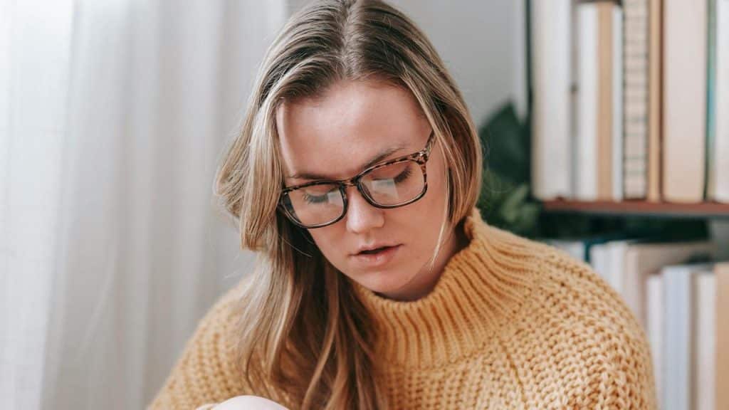 A woman wearing glasses looking down while reading indoors.