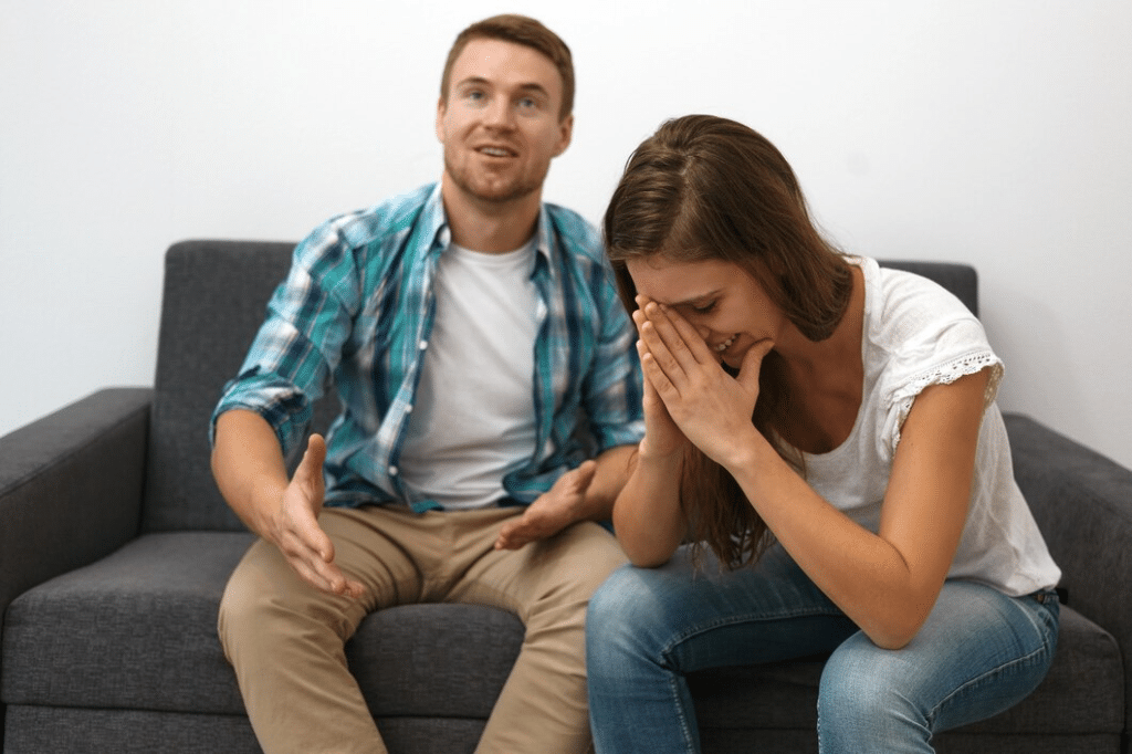 Man happy on couch, with woman holding her head in hands beside