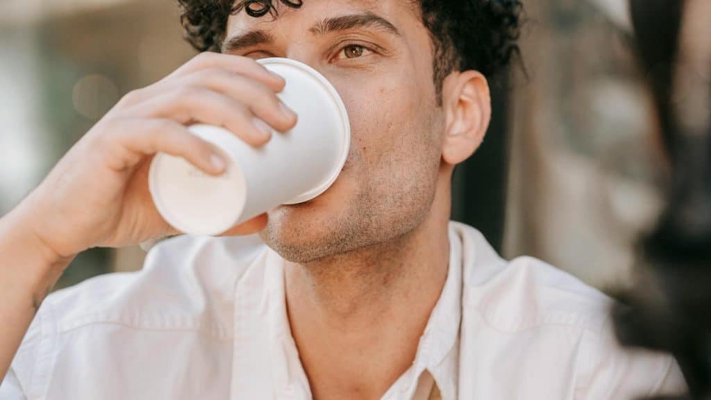 A man drinking from a paper cup outdoors.