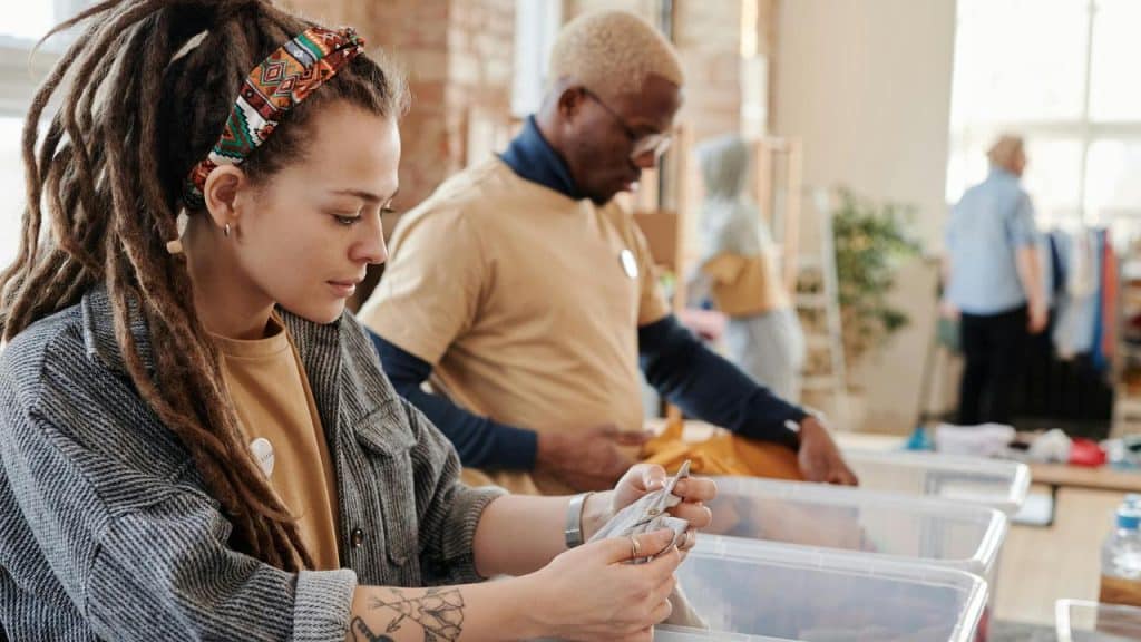 A woman sorting items into a bin while working with others in a bright indoor space.