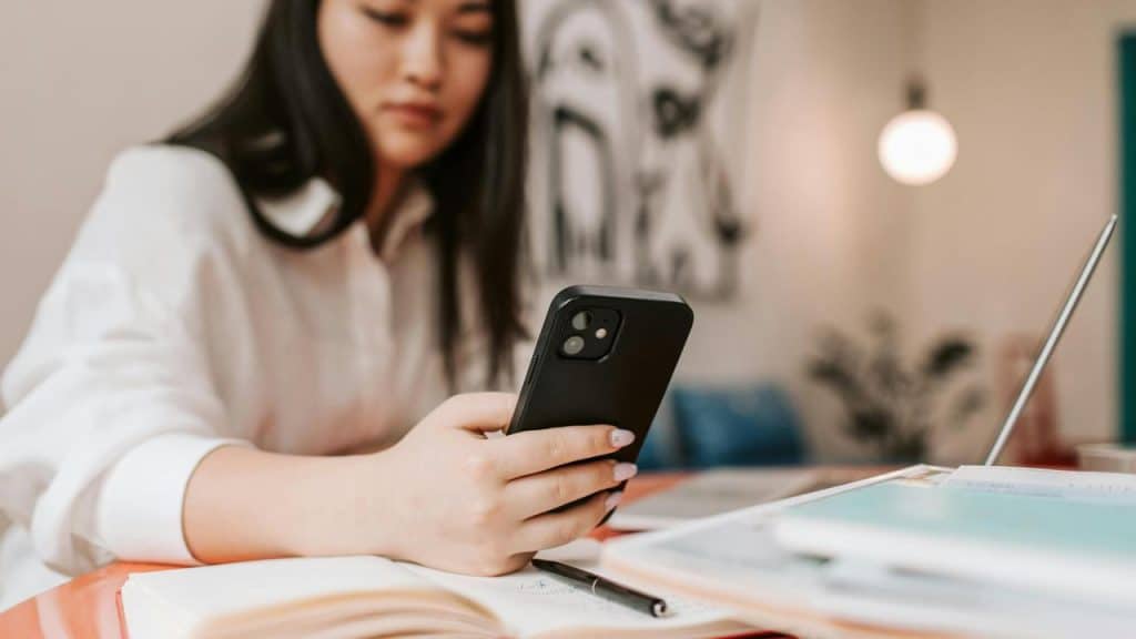 A woman looking at her phone while studying at a desk.