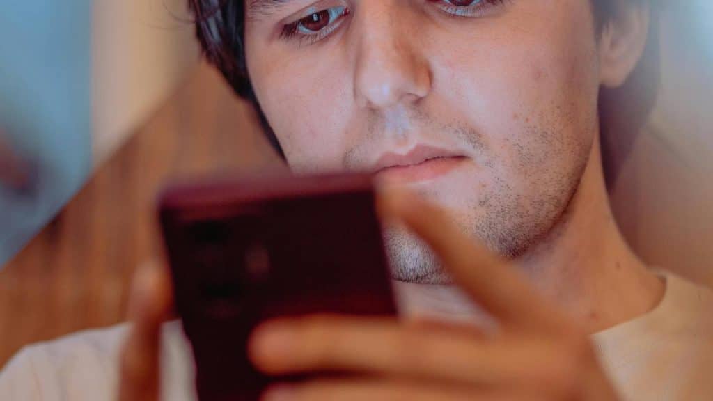 A close-up shows a person focused on a smartphone held in both hands.
