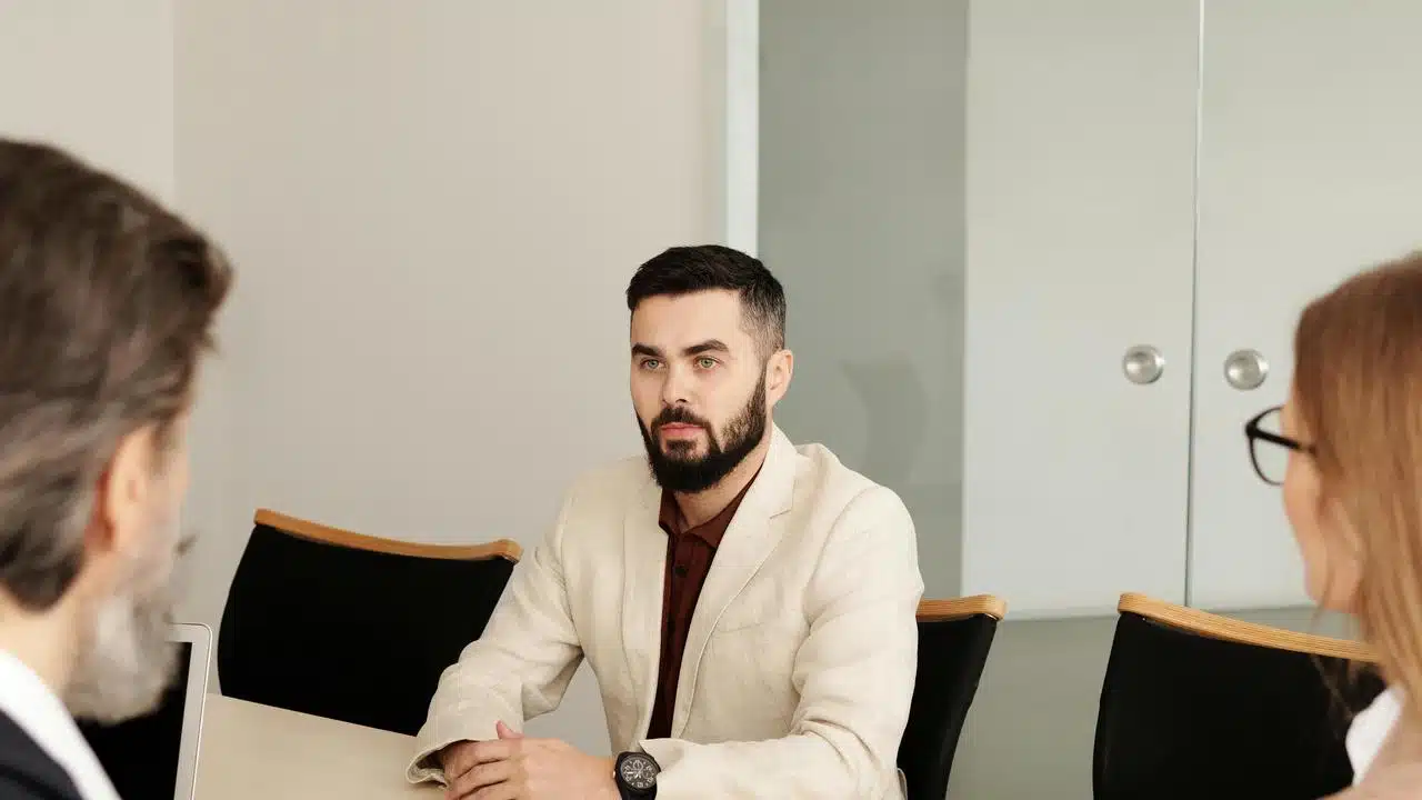 A person seated at a table during a business meeting with two others.