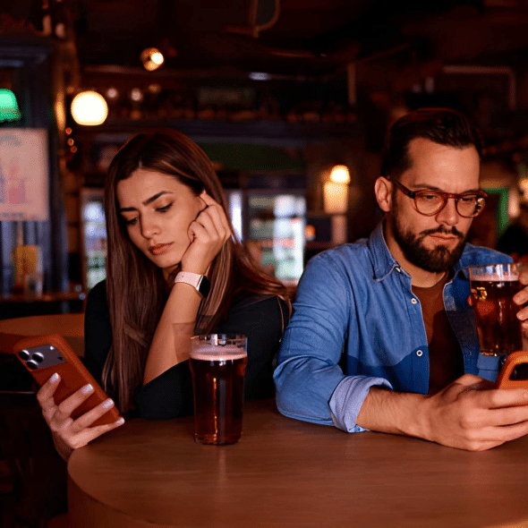 Couple at a bar table, holding smartphones and avoiding eye contact