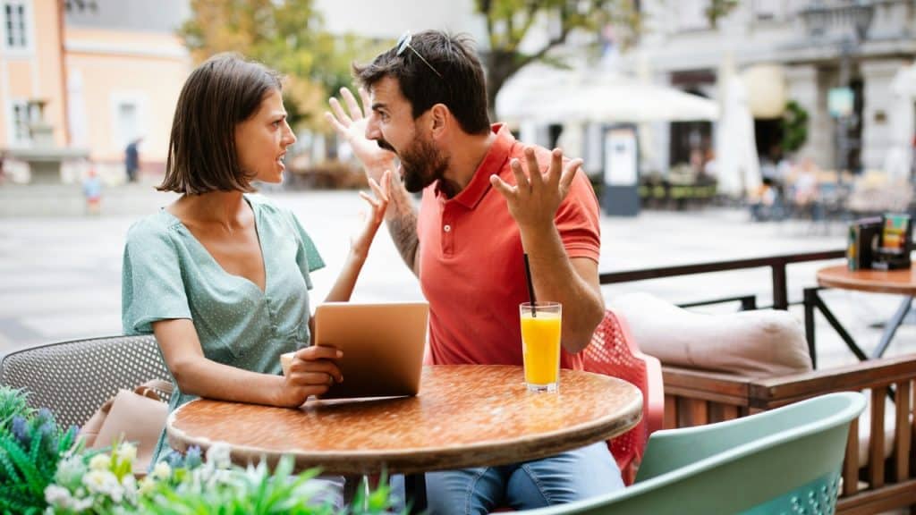 A man and woman sit at an outdoor cafe table having a spirited conversation.