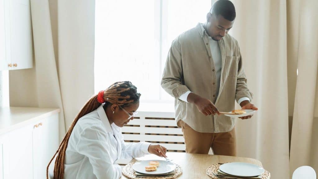 A man serving food while a woman sits at a dining table.