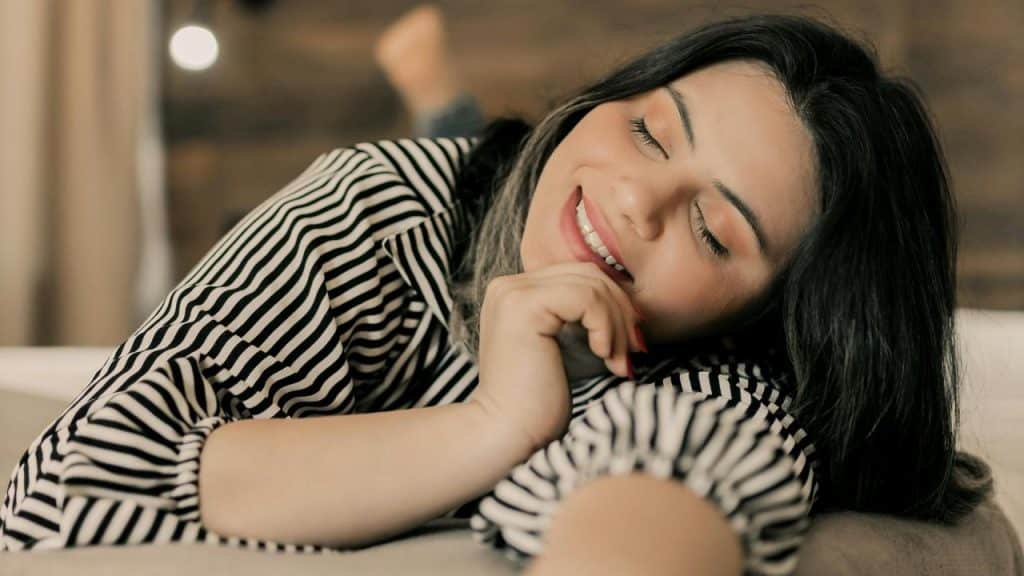 A smiling woman resting her head on her arm with eyes closed.
