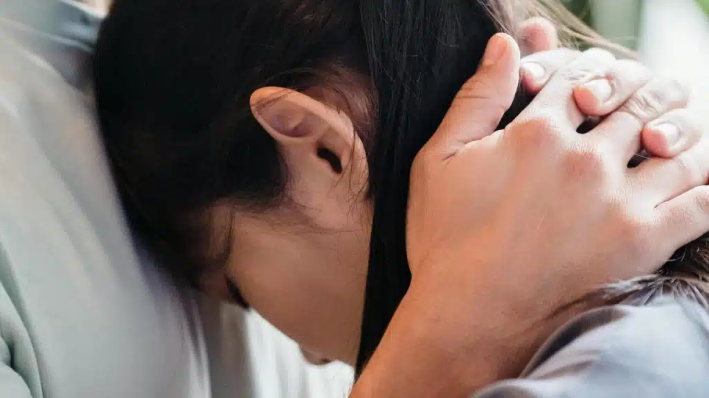 A person gently holding another person’s head in a comforting embrace