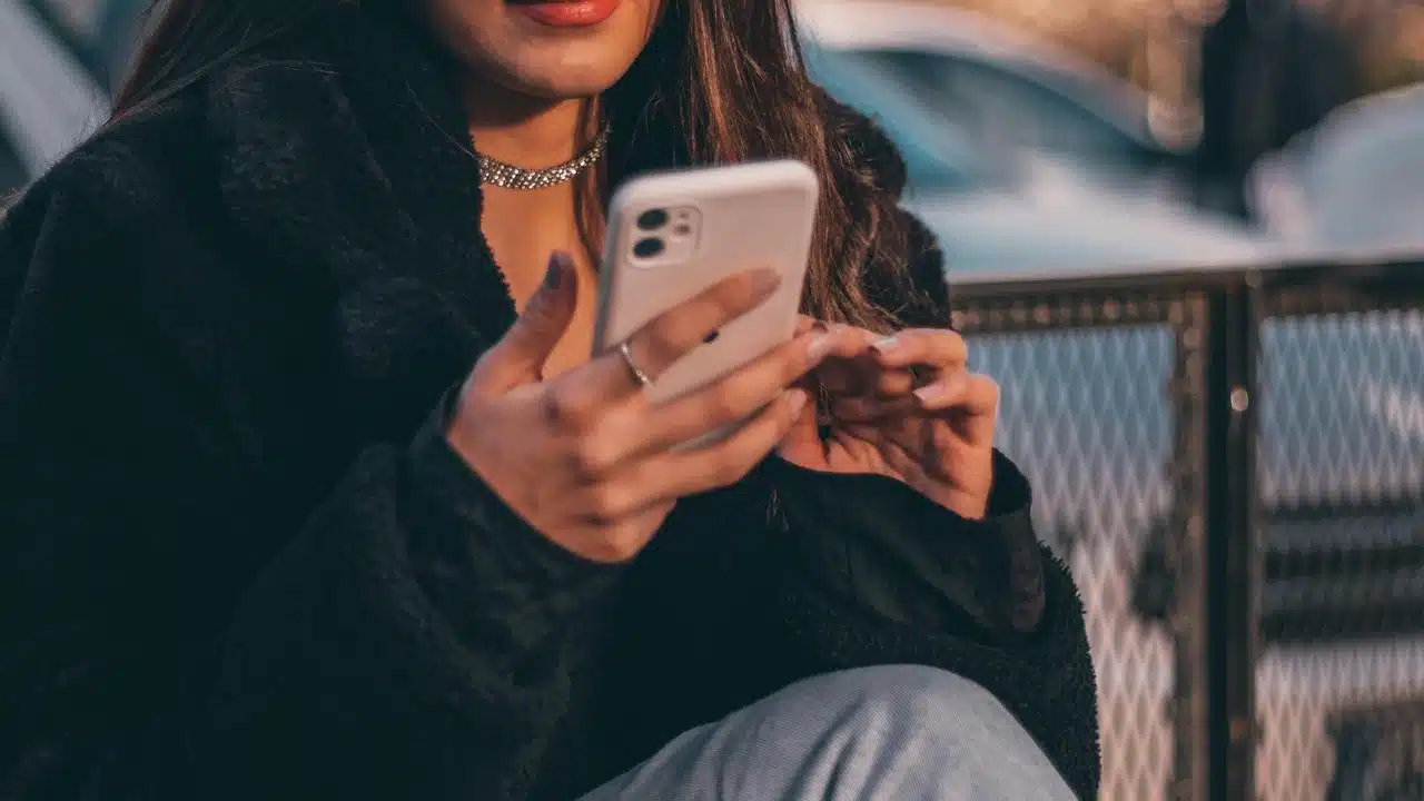 A woman holding and using a smartphone while sitting outdoors.