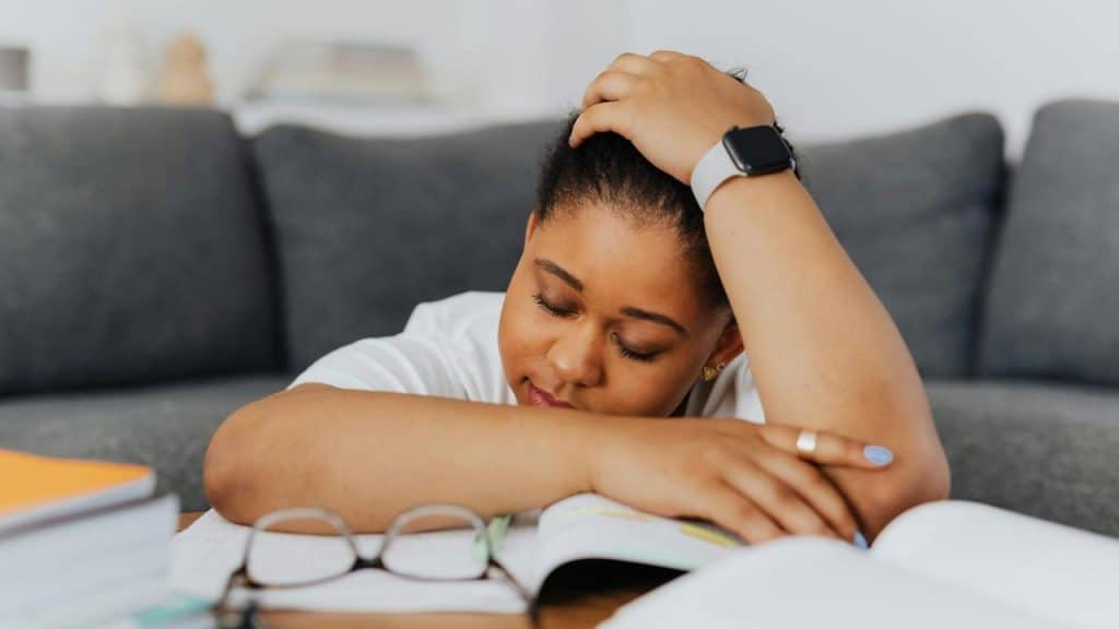 A tired woman resting her head on her arm over books while studying.