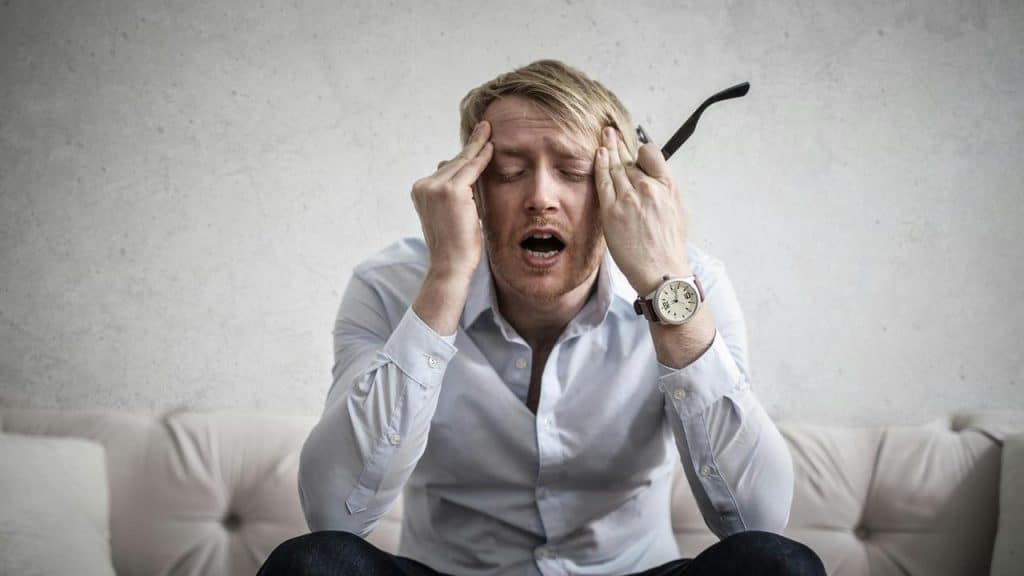 A stressed man holding his head while sitting on a couch.