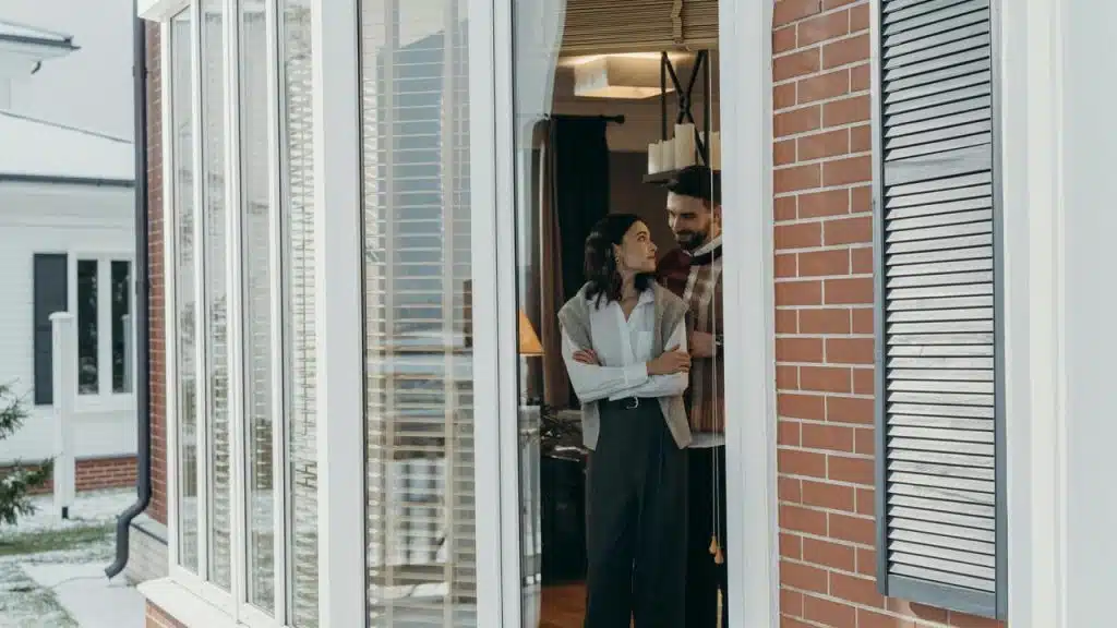 A couple standing by a window inside a cozy home, looking at each other.