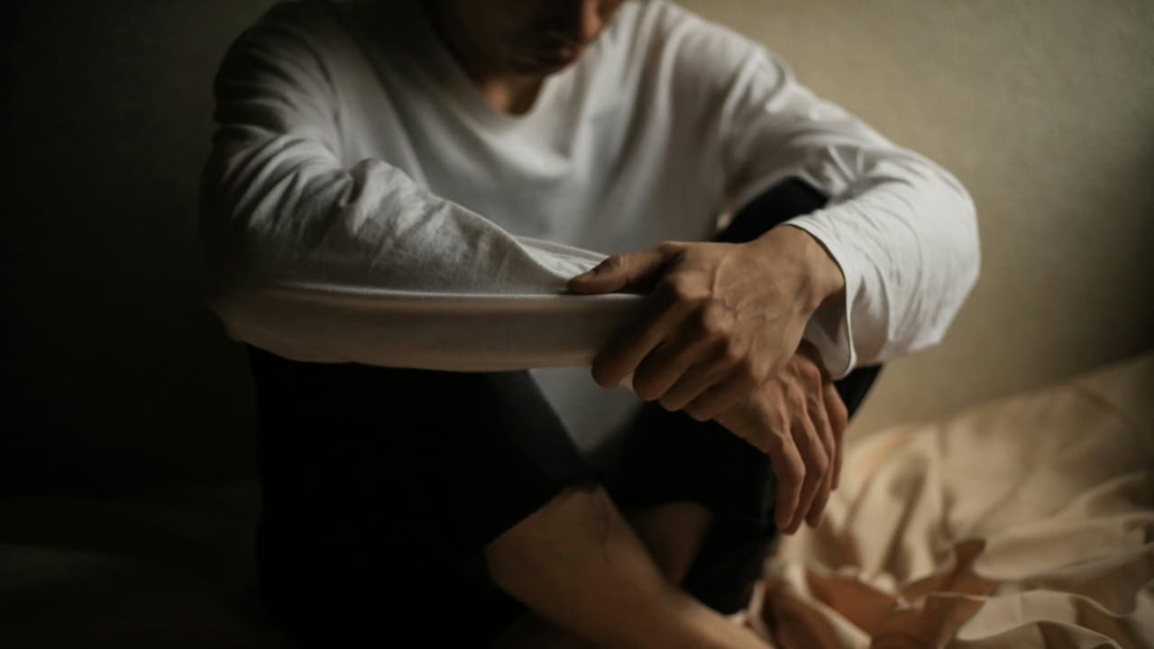 A person in a white long-sleeved shirt sits on the floor with their arms crossed over knees.