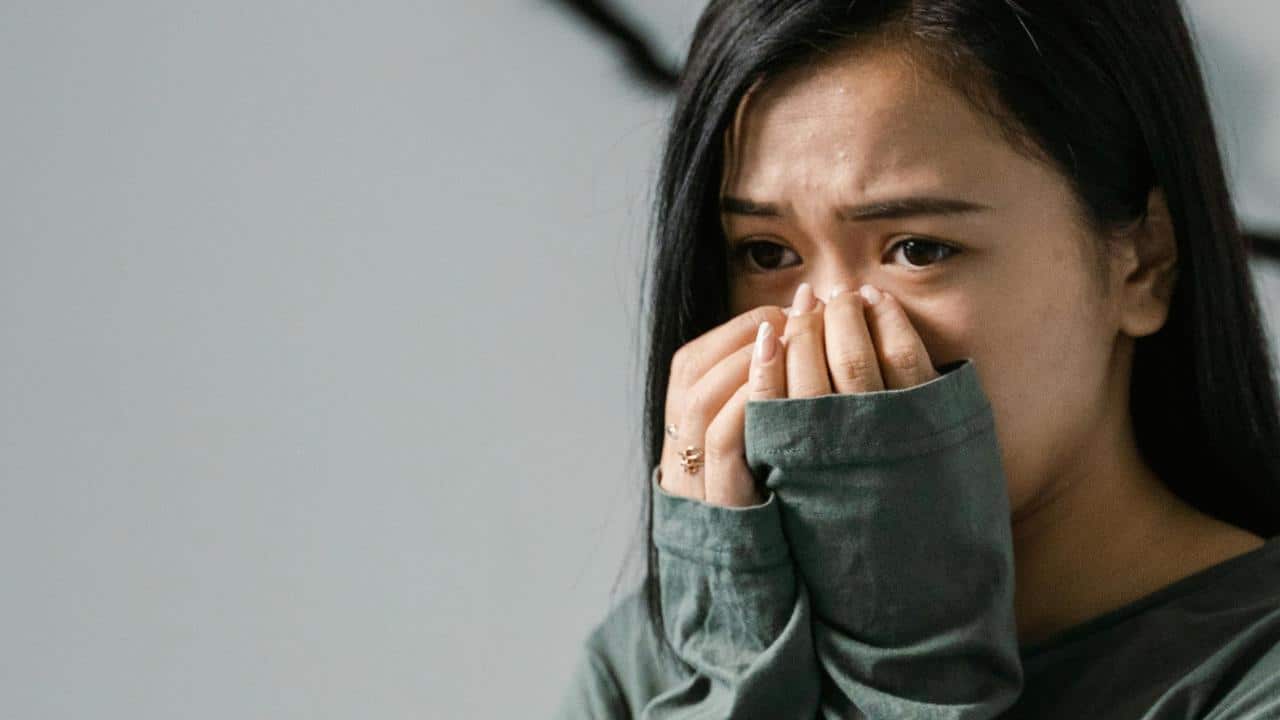 A worried woman covering her mouth with her hands, looking anxious.