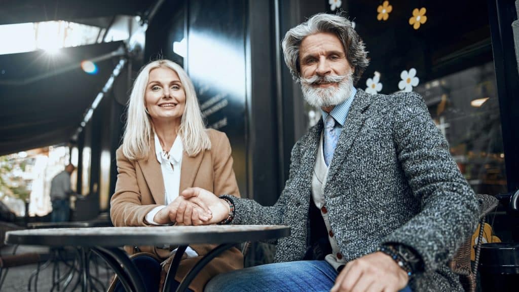 A smiling woman is sitting with a man in a cafe and holding his hand.