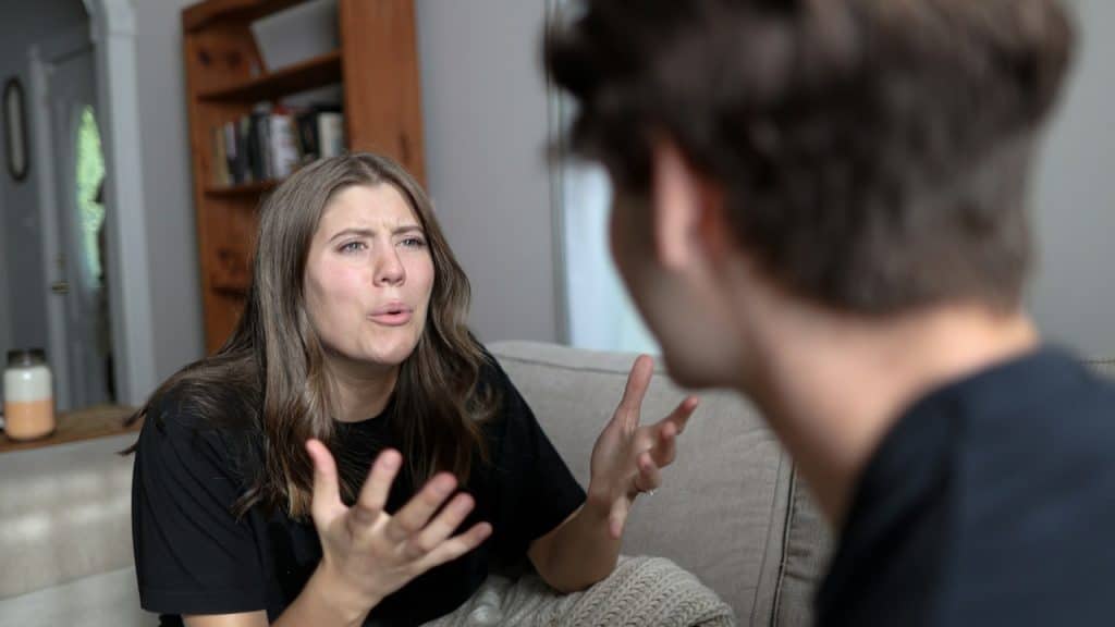 A woman gesturing intensely and arguing with a man who is partially visible in the foreground.
