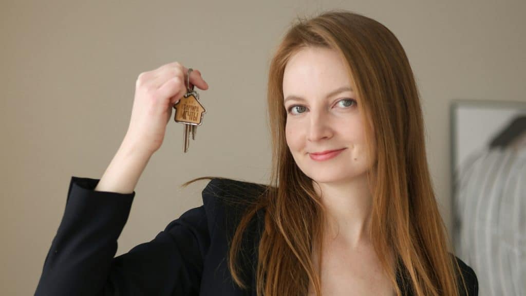 A smiling woman with long reddish hair holds up a set of keys with a keychain.