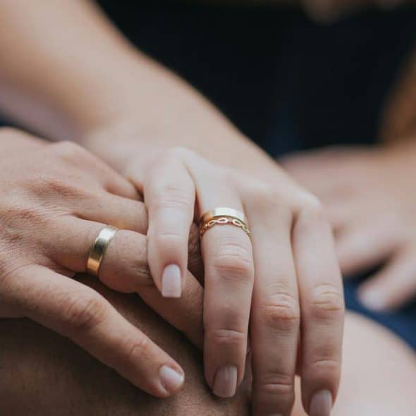 A close-up of two hands with matching rings resting together.