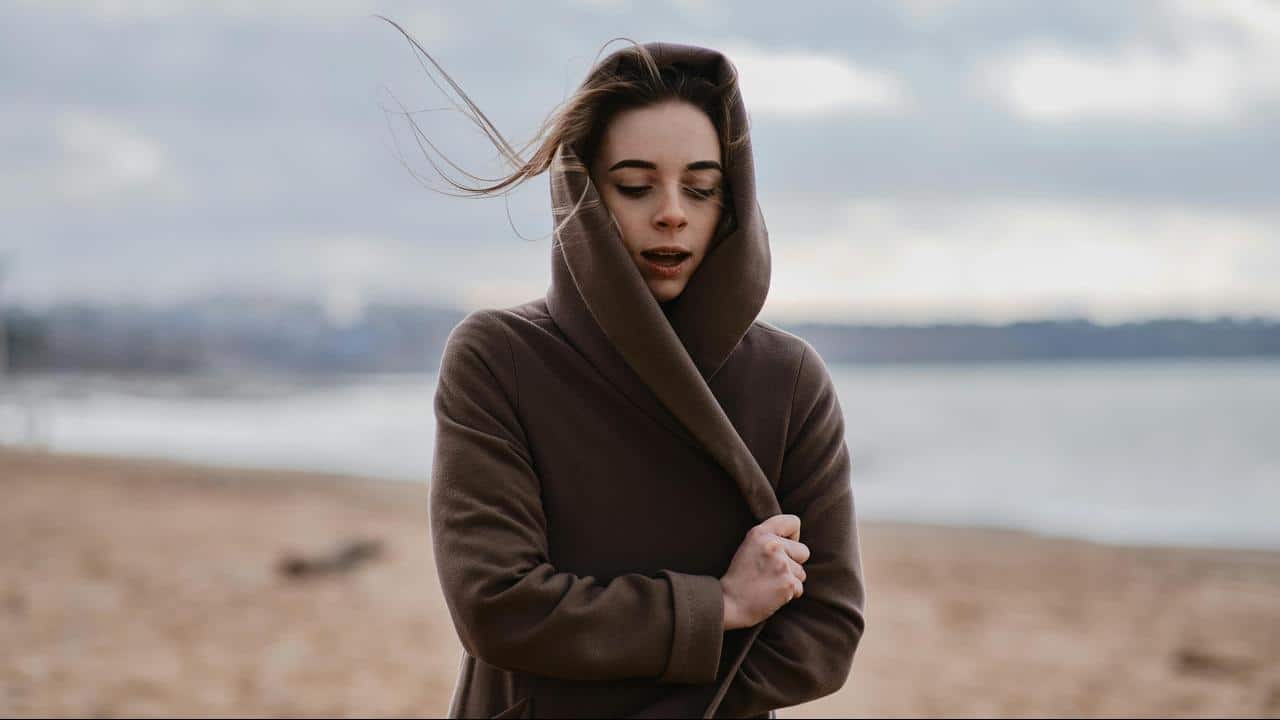A woman in a hooded coat standing on a windy beach.