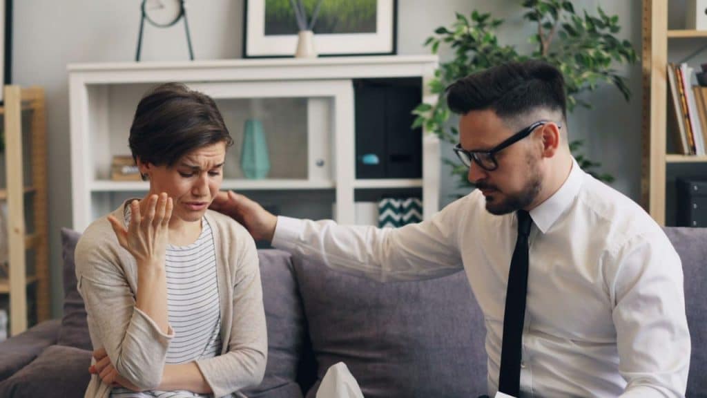 A man in a tie places a hand on the shoulder of a crying woman.