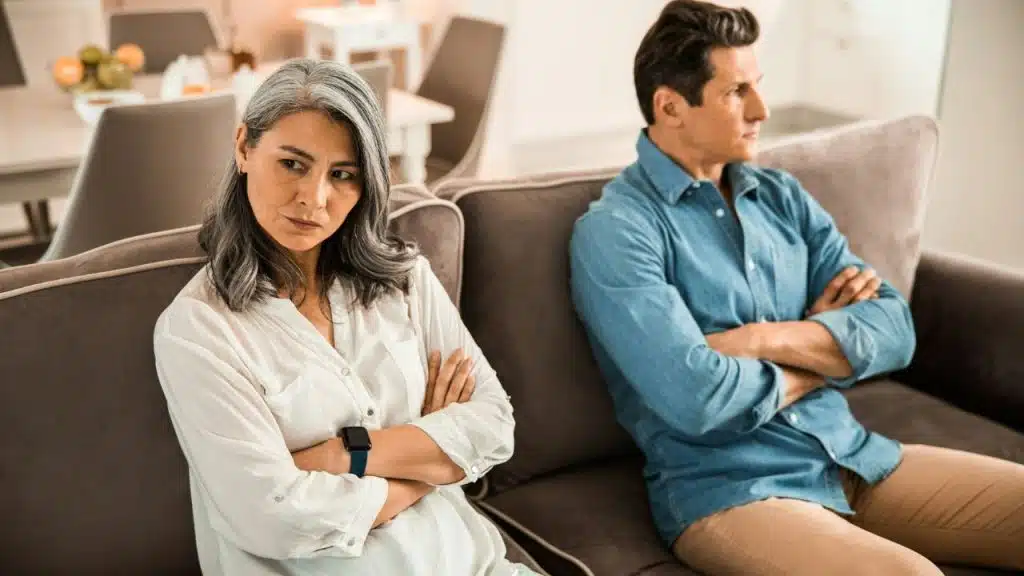 A man and woman sit on a couch with arms crossed, looking away from each other.