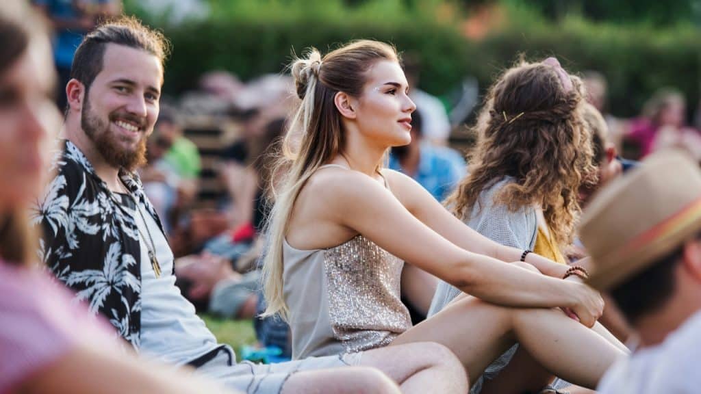 A group of people sit on the grass outdoors, looking toward the right side.