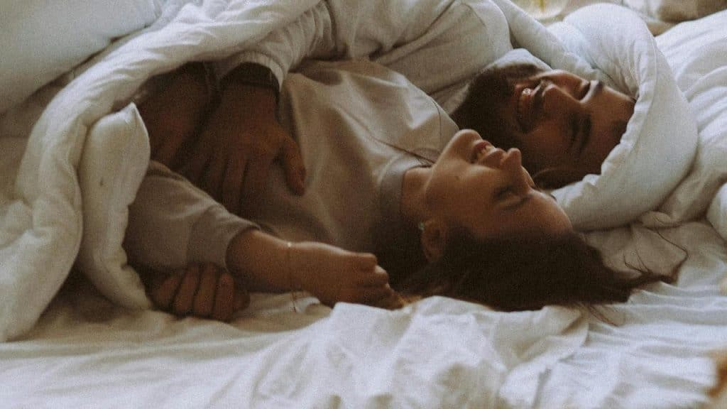 A couple lying in bed smiling and cuddling.