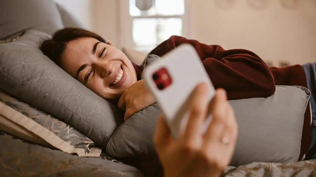 A smiling woman lying on a couch while looking at her phone.