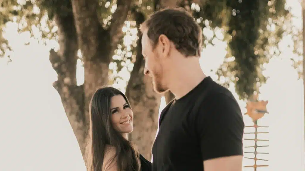 A man and a woman standing next to each other in front of a tree.