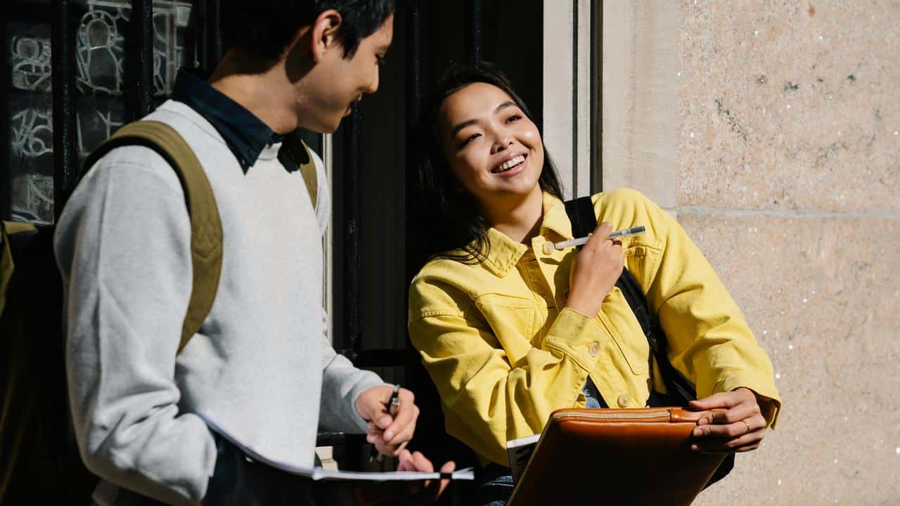 A smiling woman in a yellow jacket chatting with a guy outside.