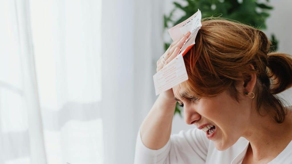 A woman holding papers to her head, looking stressed and overwhelmed.