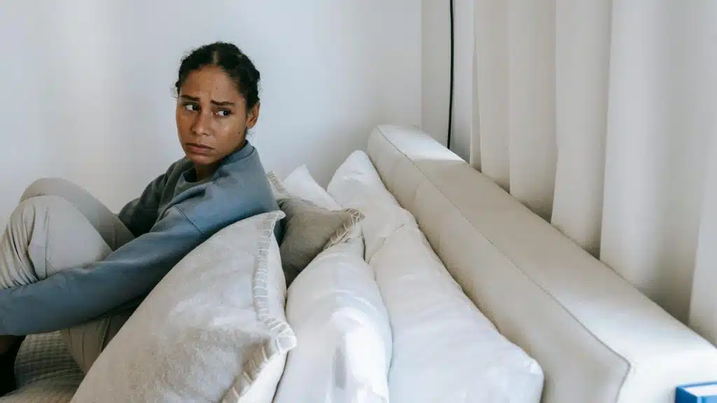 A woman sitting on a bed with pillows, looking worried and turned away.