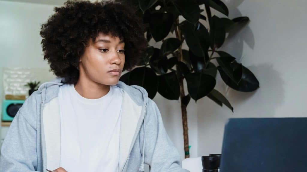 A woman looking at a laptop with a focused expression while sitting indoors.