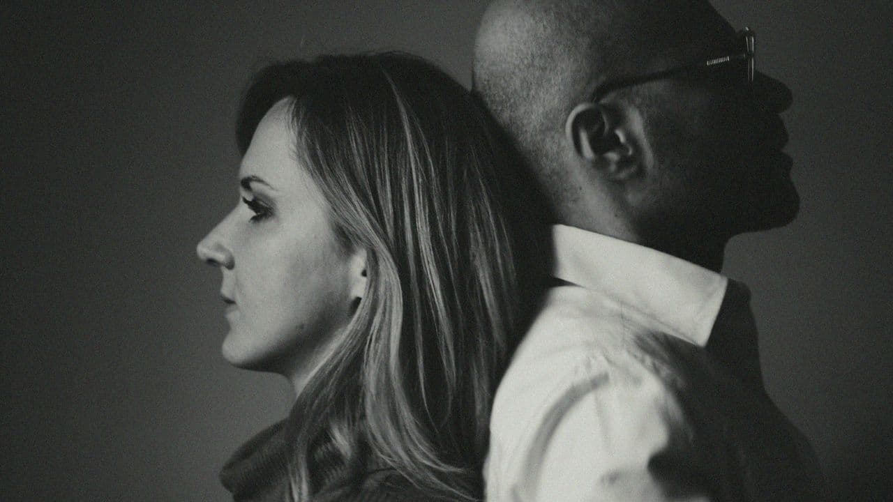 A black and white profile photo of a woman and man leaning back to back.