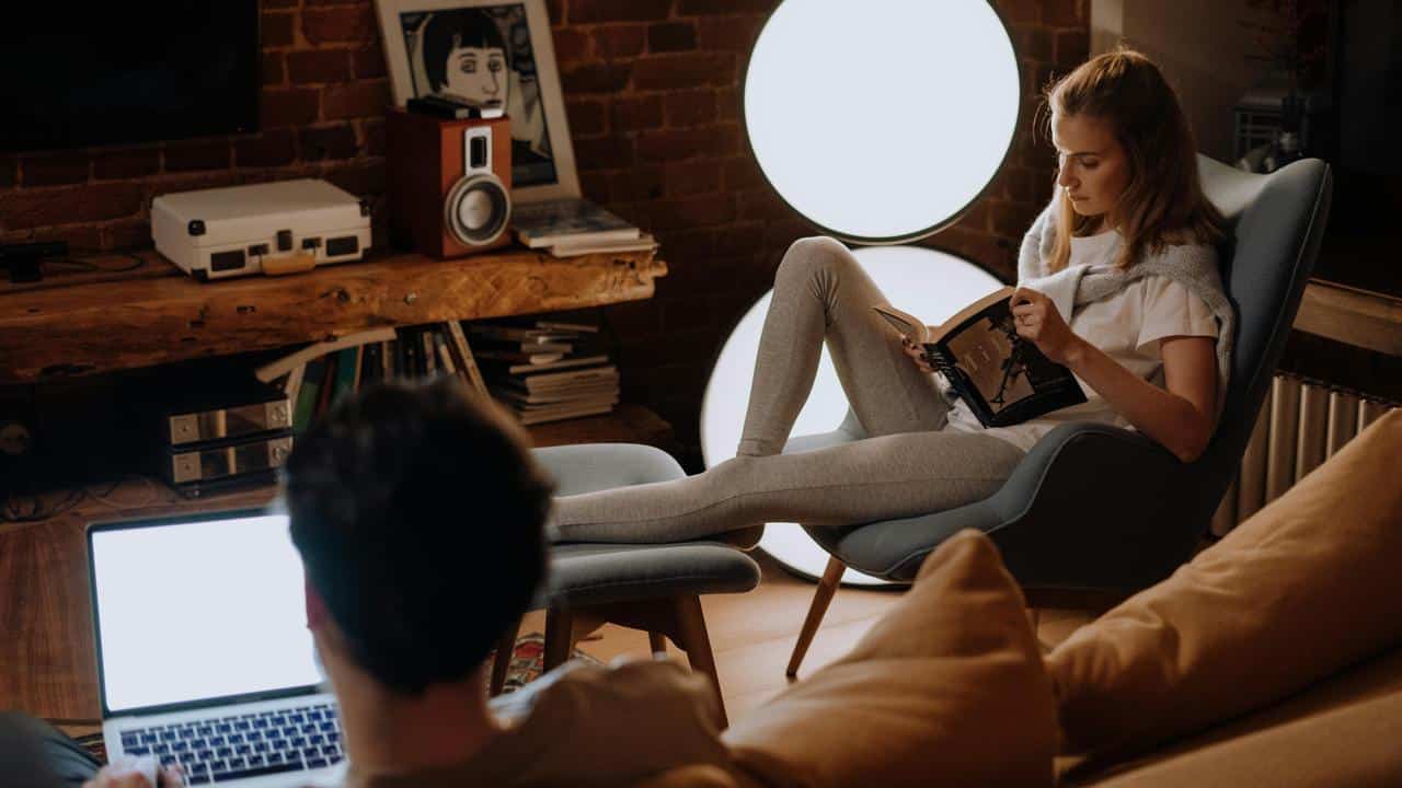 A woman reads in a chair while a man uses a laptop