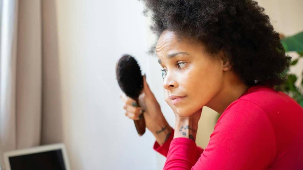 A woman holding a hairbrush while looking at herself with a concerned expression.