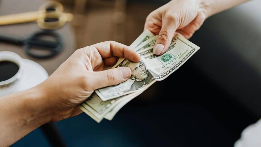 A person handing cash to another person across a table.
