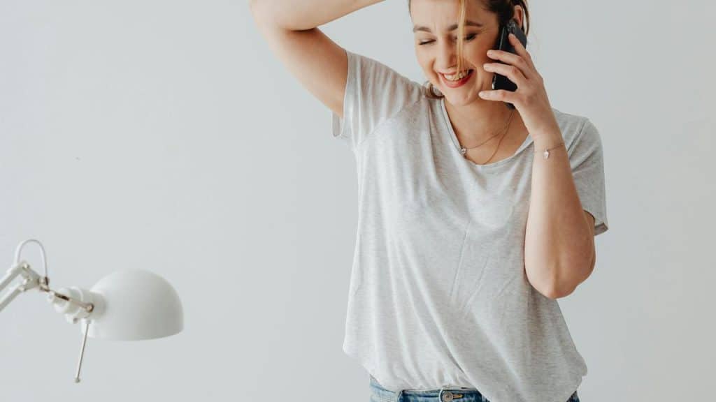 A smiling woman talking on a smartphone while holding her head.