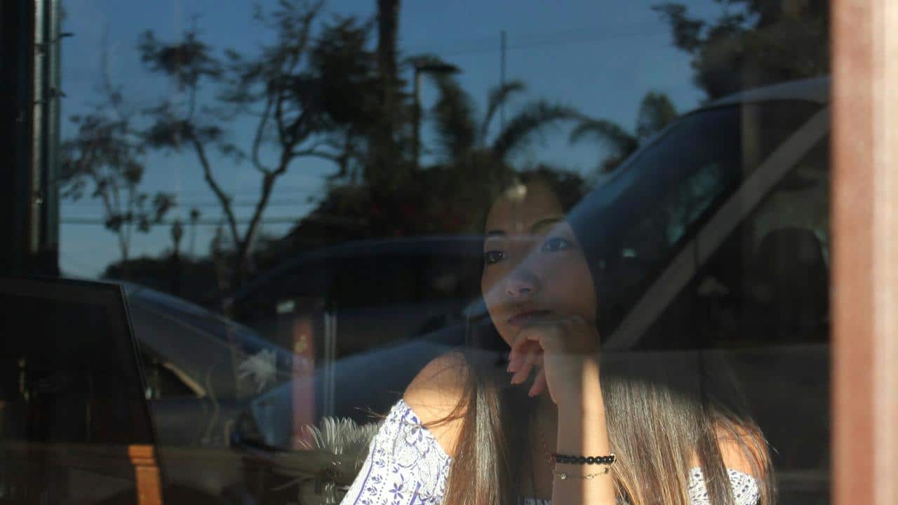 A woman gazing thoughtfully out a window with reflections around her.