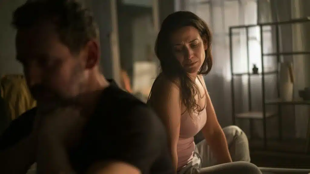 A woman in a pink tank top looks toward a man who is blurred in the foreground.