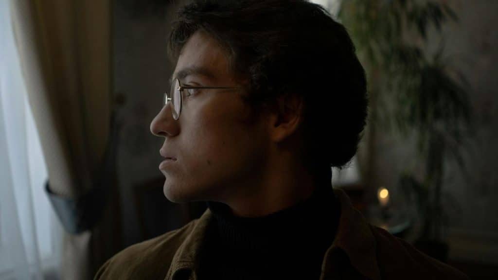 A man wearing glasses looking out a window.