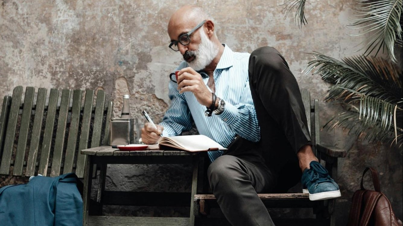 A man taking notes in a planner and drinking coffee in the street.