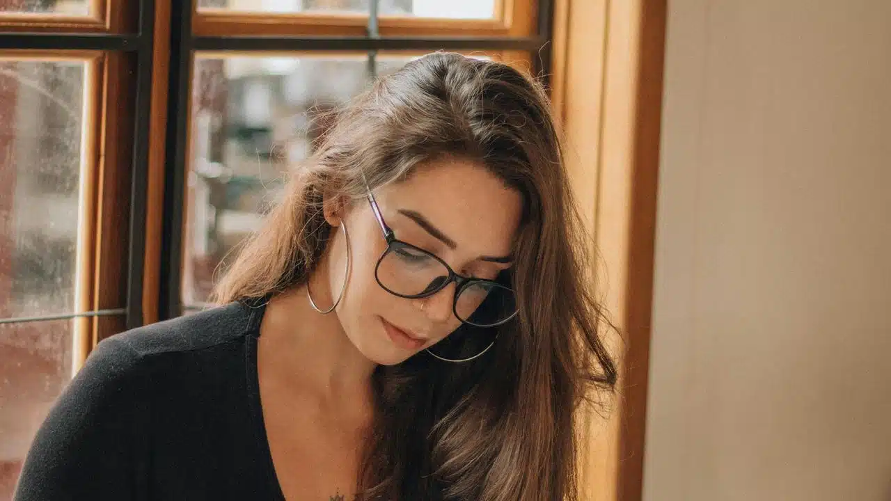 A woman wearing glasses looking down indoors.