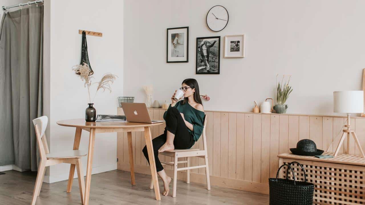 A woman drinking coffee while sitting at a table with a laptop at home.