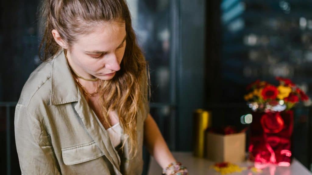 A woman looking down while working at a table with flowers and decorations nearby.