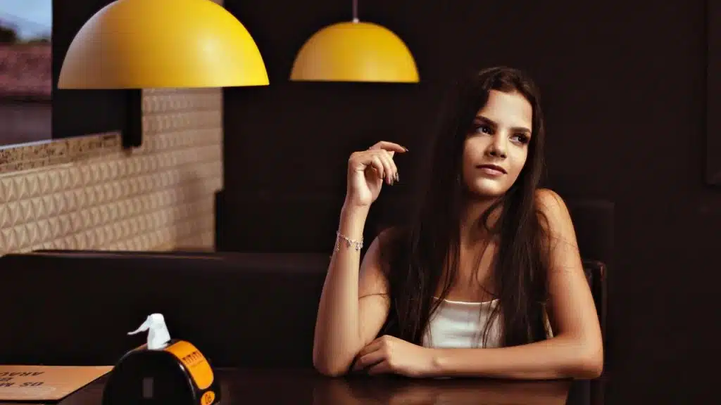 A woman sitting thoughtfully at a restaurant table under warm lighting.