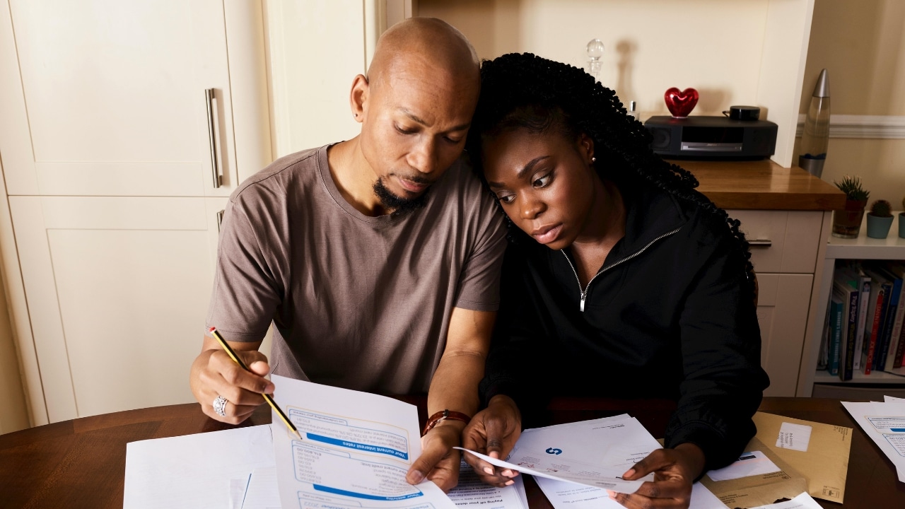 A man and woman sit at a table closely reviewing several financial documents and papers.