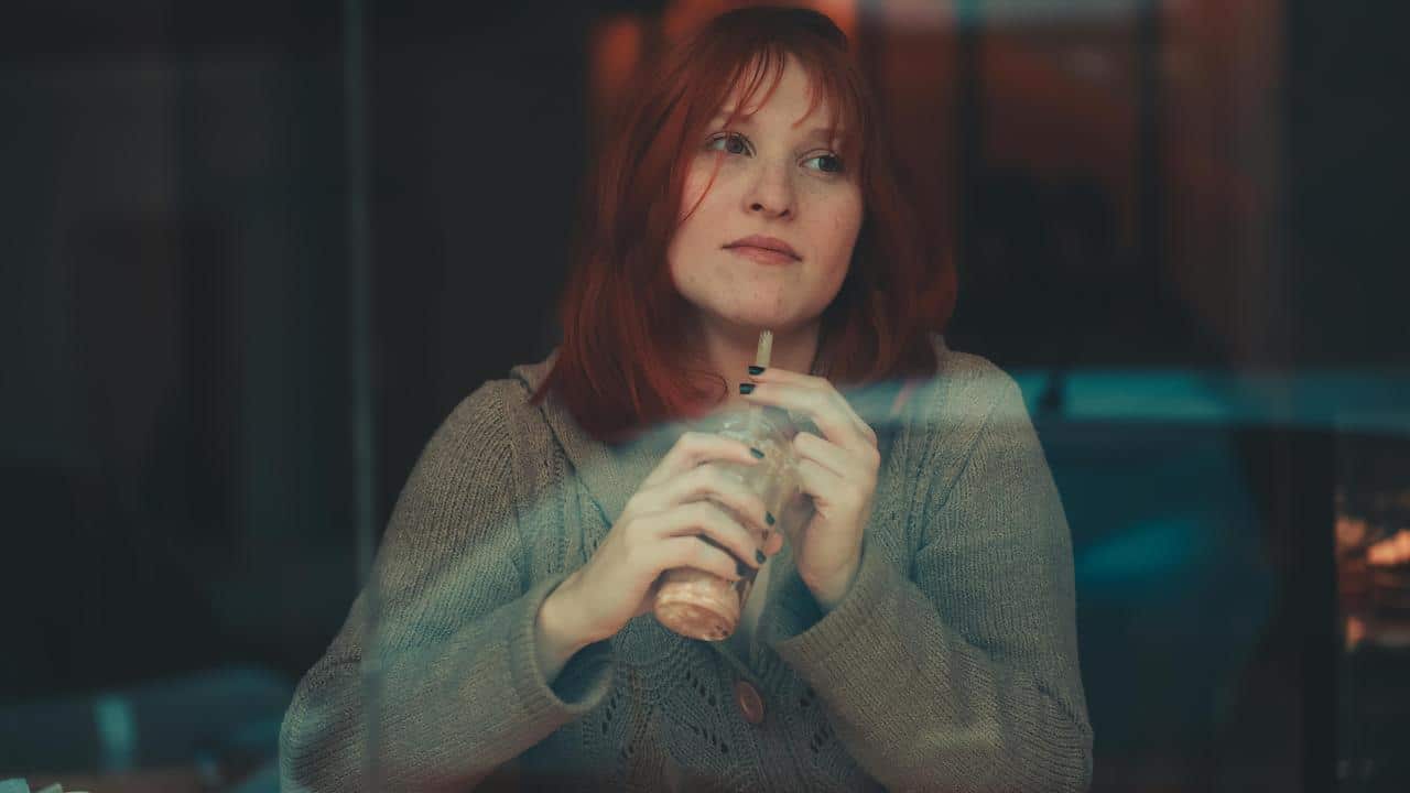 A woman holding a drink and looking thoughtfully through a window.
