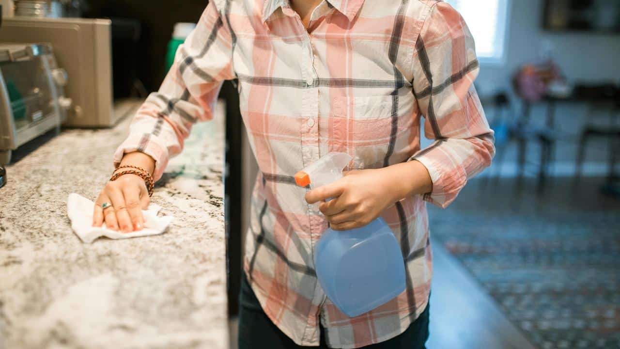 A person cleaning a kitchen countertop with a cloth and spray bottle.