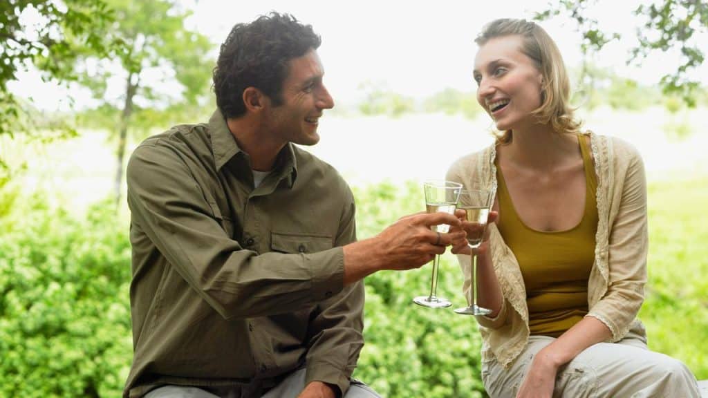 A couple clinking wine glasses while smiling together outdoors.
